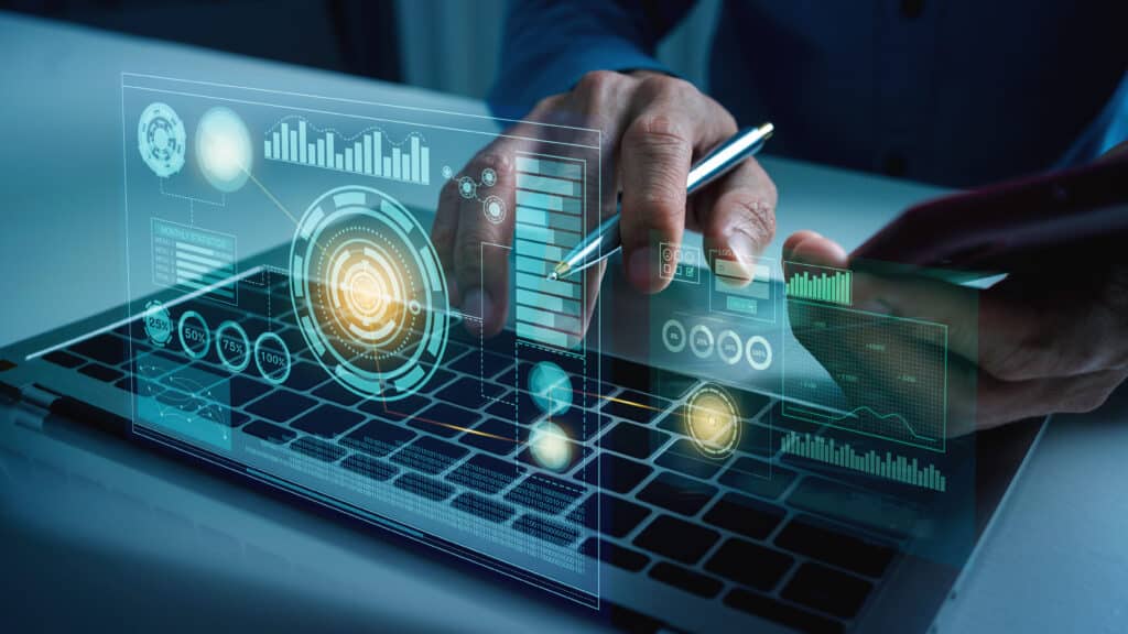 A person using a laptop with digital data graphics and futuristic interface holograms projected above the keyboard, showing charts, graphs, and analytics.