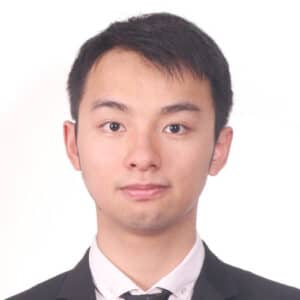 A young man with short black hair wearing a black suit, white shirt, and black tie, facing forward and looking at the camera with a neutral expression against a plain white background.