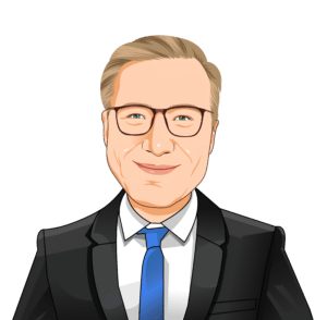 Illustration of a man with blond hair wearing glasses, a black suit, white shirt, and blue tie, smiling and facing forward against a plain background.