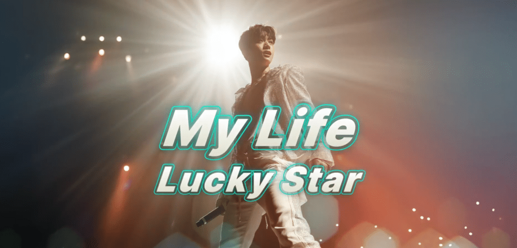 A performer stands on stage under bright lights, holding a microphone, with the text My Life Lucky Star in bold, teal letters across the image.